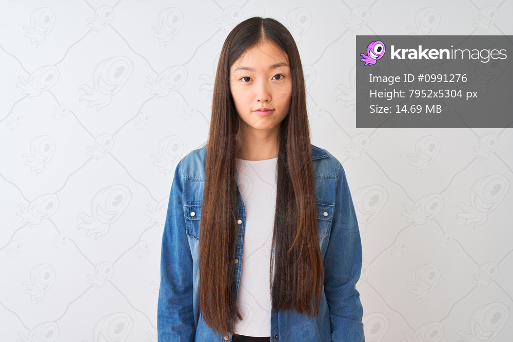 Young chinese woman wearing denim shirt standing over isolated white background Relaxed with serious expression on face. Simple and natural looking at the camera.