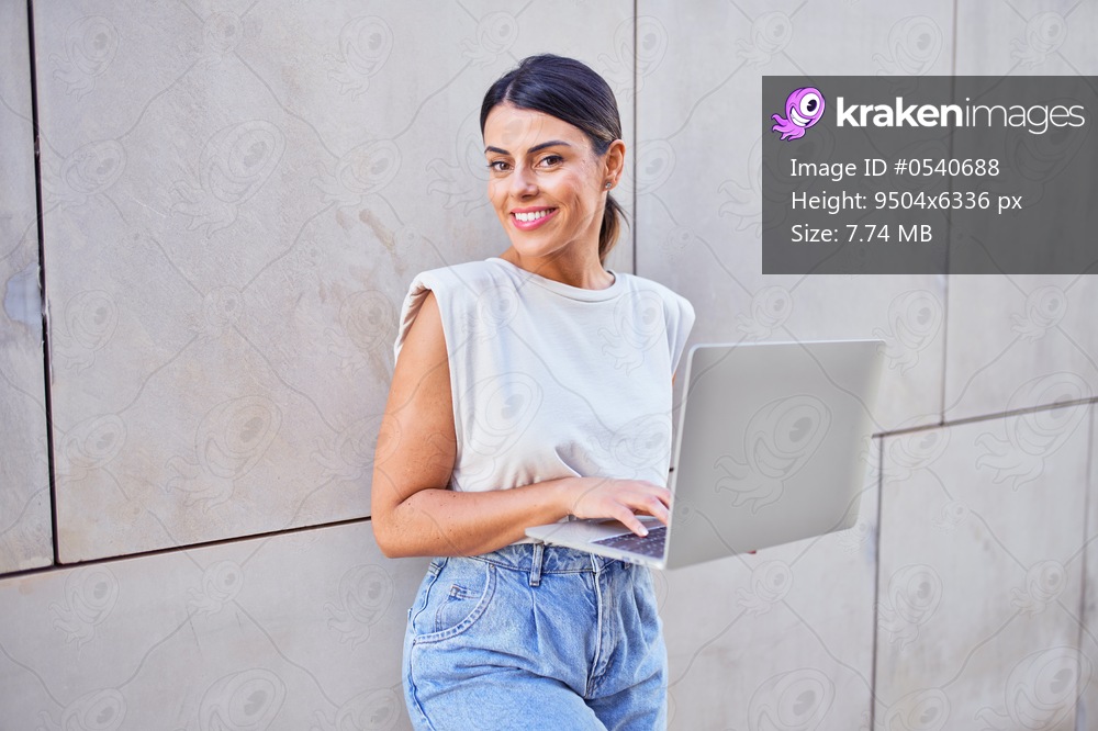 Beautiful young woman wearing fashionable clothes walking down the street and working using computer laptop