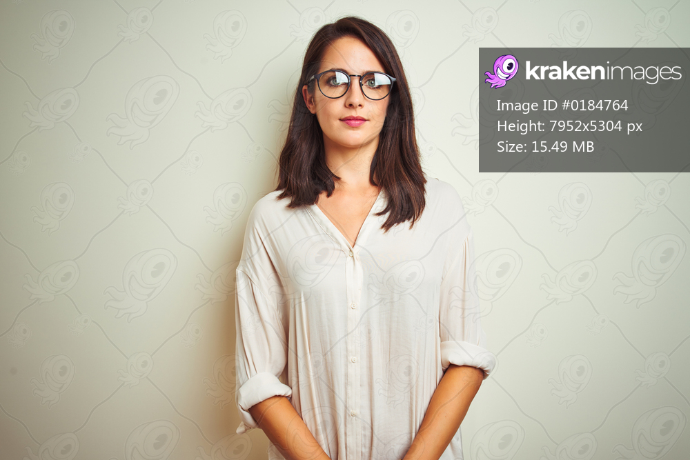 Young beautiful woman wearing shirt and glasses standing over white isolated background smiling in love showing heart symbol and shape with hands. Romantic concept.