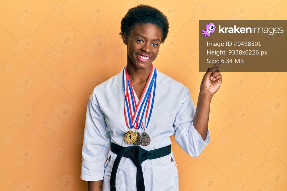 Young african american girl wearing karate kimono and black belt smiling happy pointing with hand and finger to the side 