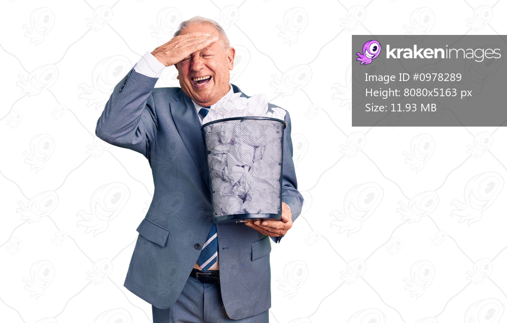 Senior handsome grey-haired man holding paper bin with crumpled document stressed and frustrated with hand on head, surprised and angry face 