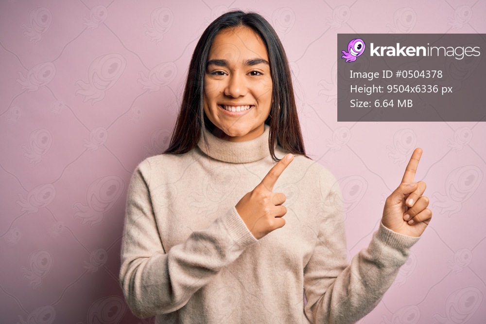 Young beautiful asian woman wearing casual turtleneck sweater over pink background smiling and looking at the camera pointing with two hands and fingers to the side.