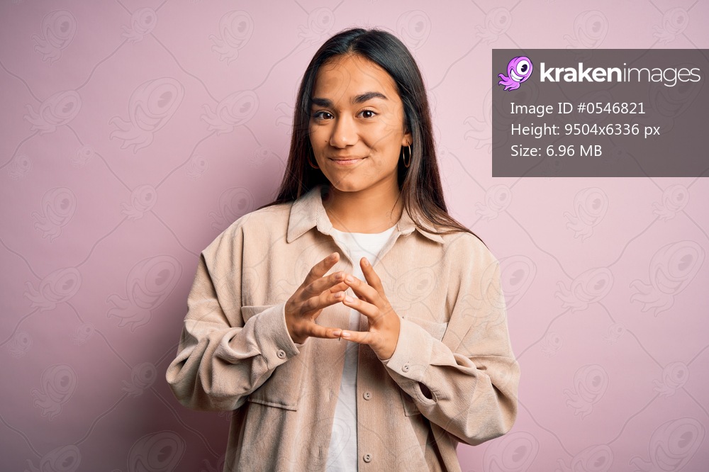 Young beautiful asian woman wearing casual shirt standing over pink background Hands together and fingers crossed smiling relaxed and cheerful. Success and optimistic
