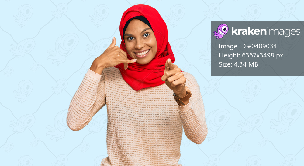 Young african american woman wearing traditional islamic hijab scarf smiling doing talking on the telephone gesture and pointing to you. call me. 