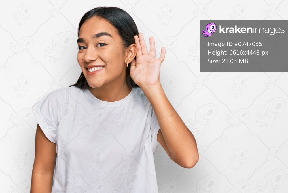 Young asian woman wearing casual white t shirt smiling with hand over ear listening an hearing to rumor or gossip. deafness concept. 