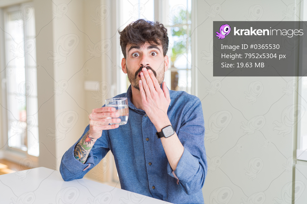 Young man drinking a fresh glass of water cover mouth with hand shocked with shame for mistake, expression of fear, scared in silence, secret concept