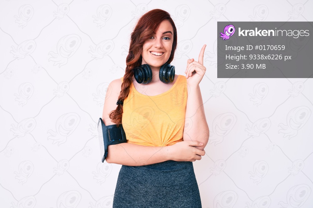 Young beautiful woman wearing gym clothes and using headphones smiling happy pointing with hand and finger to the side 