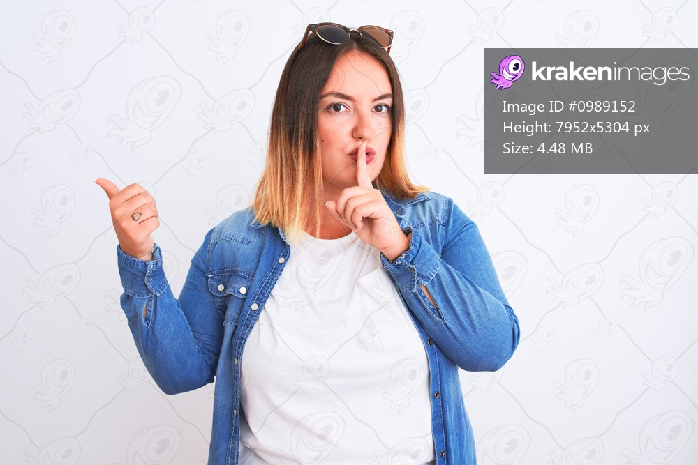 Beautiful woman wearing denim shirt standing over isolated white background asking to be quiet with finger on lips pointing with hand to the side. Silence and secret concept.