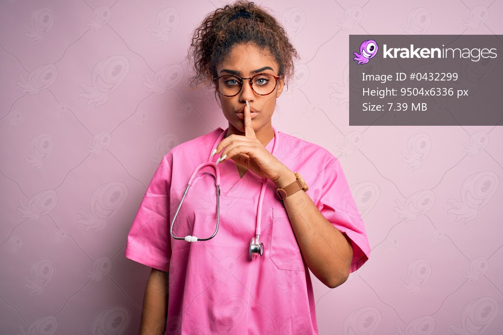 African american nurse girl wearing medical uniform and stethoscope over pink background asking to be quiet with finger on lips. Silence and secret concept.