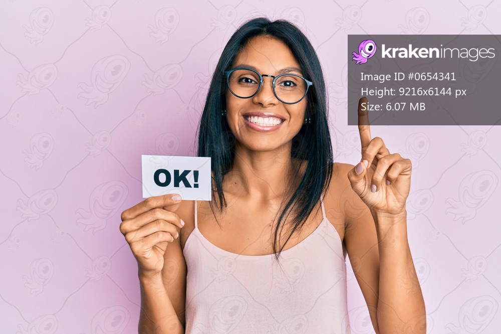 Young african american woman holding ok message paper smiling with an idea or question pointing finger with happy face, number one 