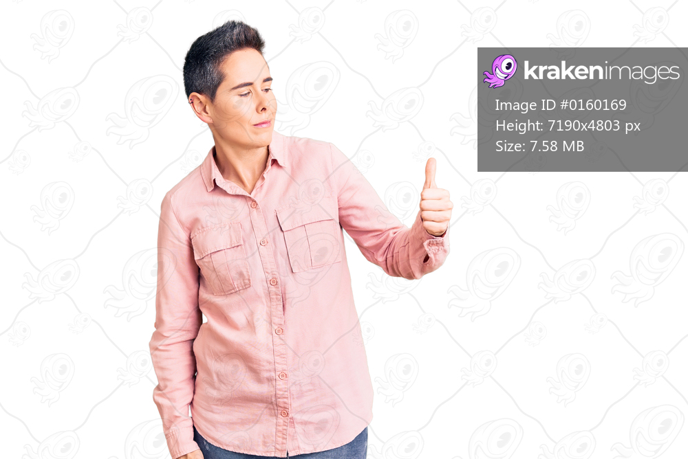 Young woman with short hair wearing casual clothes looking proud, smiling doing thumbs up gesture to the side 