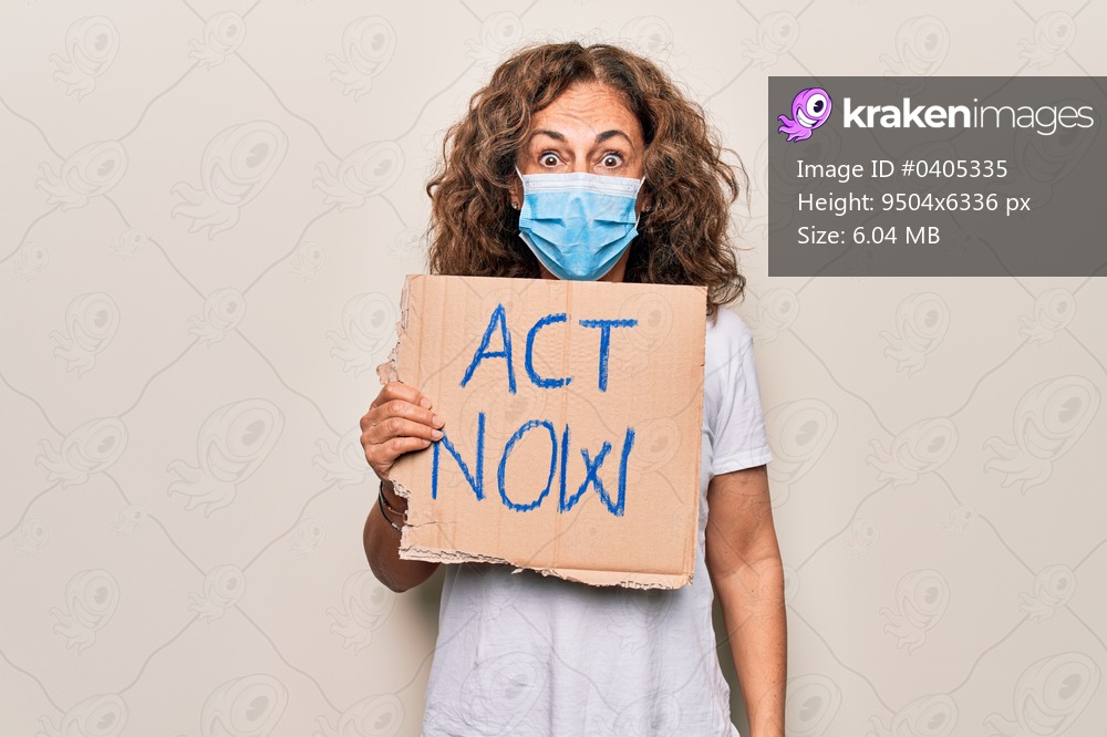 Middle age woman wearing coronavirus protection mask holding act now protest cardboard scared and amazed with open mouth for surprise, disbelief face