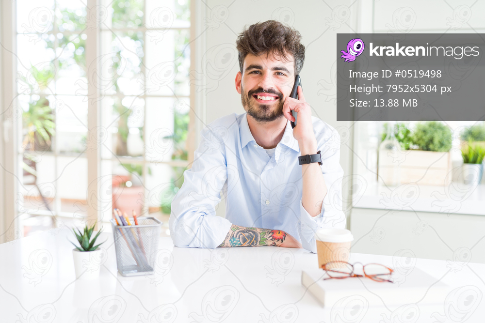 Young business man talking on smartphone with a happy face standing and smiling with a confident smile showing teeth