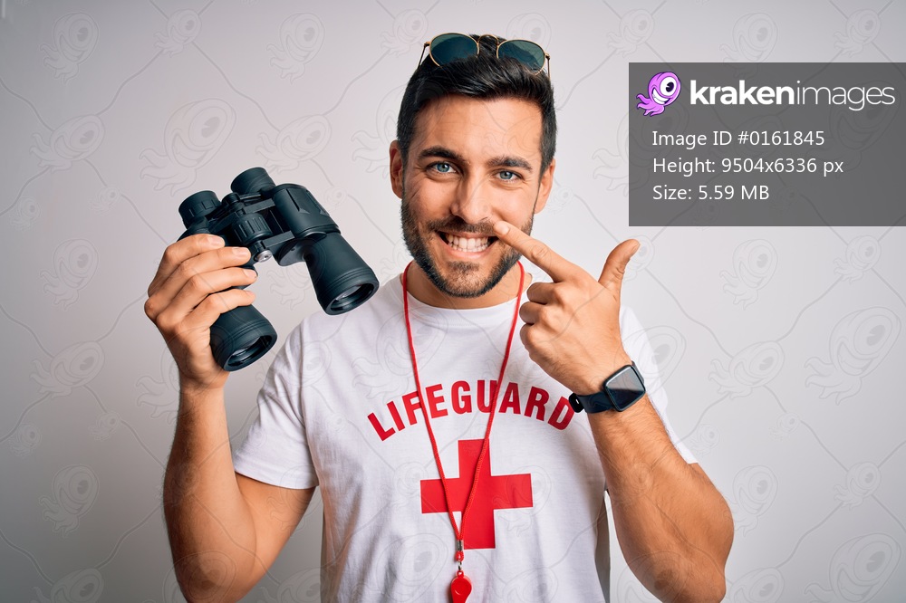 Young lifeguard man with beard wearing t-shirt with red cross and sunglasses using whistle Pointing with hand finger to face and nose, smiling cheerful. Beauty concept