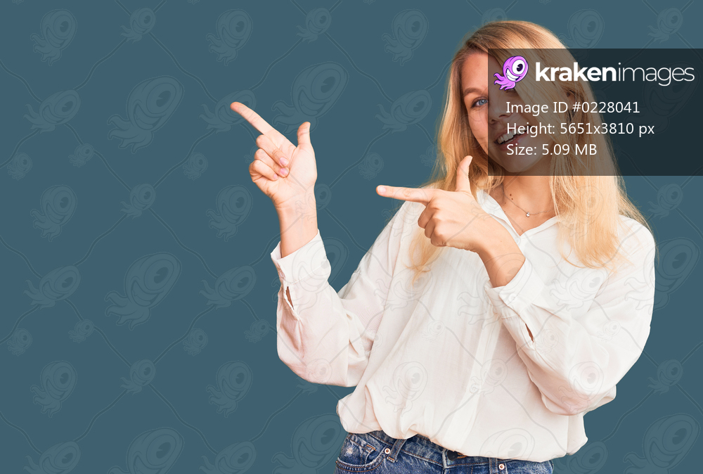 Young beautiful blonde woman wearing casual shirt smiling and looking at the camera pointing with two hands and fingers to the side. 