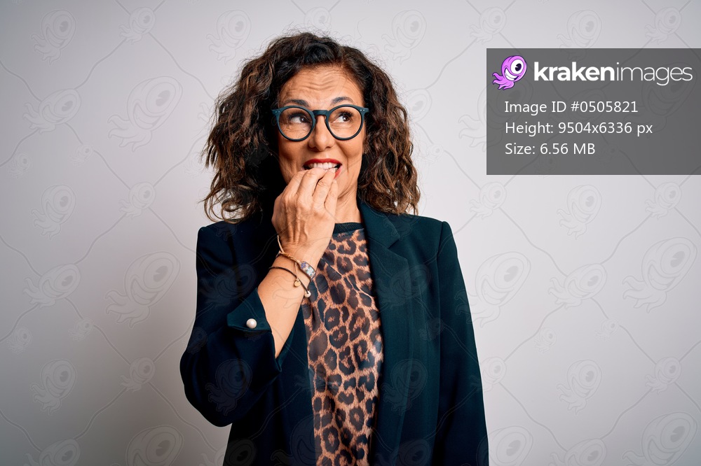 Middle age brunette business woman wearing glasses standing over isolated white background looking stressed and nervous with hands on mouth biting nails. Anxiety problem.