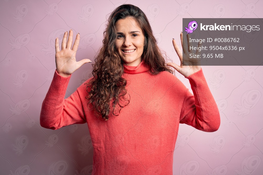 Young beautiful woman with curly hair wearing turtleneck sweater over pink background showing and pointing up with fingers number ten while smiling confident and happy.