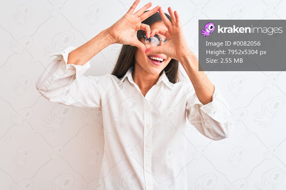 Young beautiful businesswoman wearing glasses standing over isolated white background Doing heart shape with hand and fingers smiling looking through sign