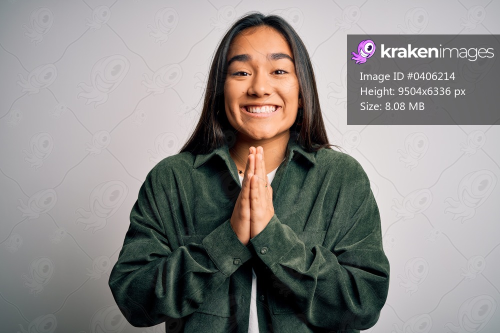 Young beautiful asian woman wearing casual shirt standing over isolated white background praying with hands together asking for forgiveness smiling confident.