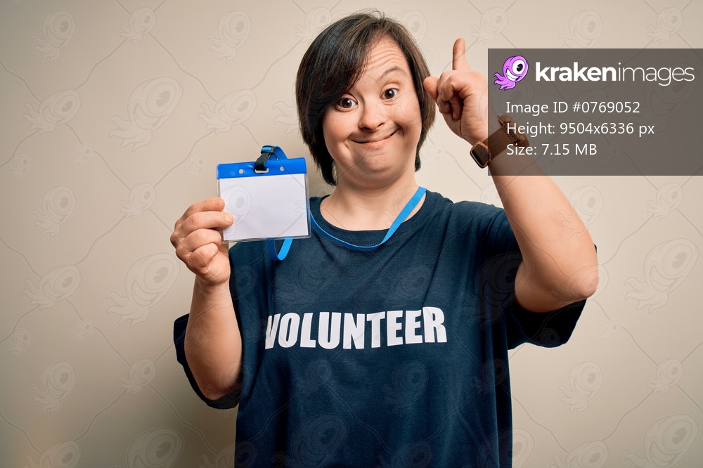 Young down syndrome volunteer woman wearing social care charity t-shirt showing identification surprised with an idea or question pointing finger with happy face, number one