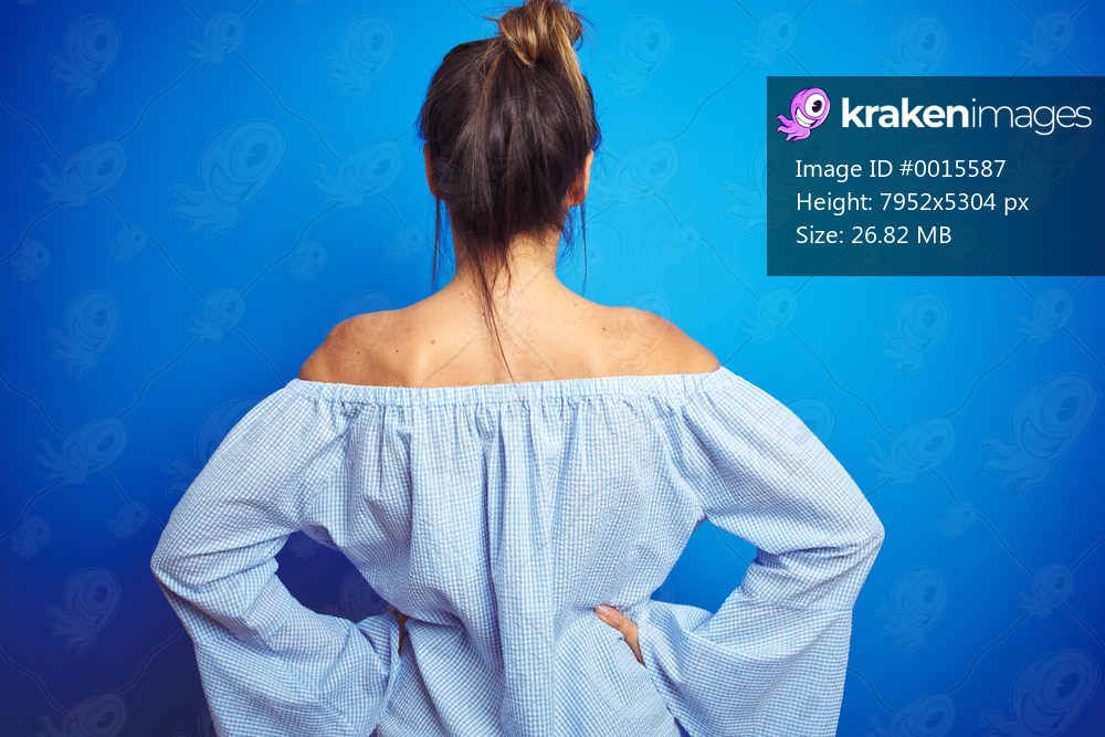 Young beautiful woman wearing bun hairstyle over blue isolated background standing backwards looking away with arms on body