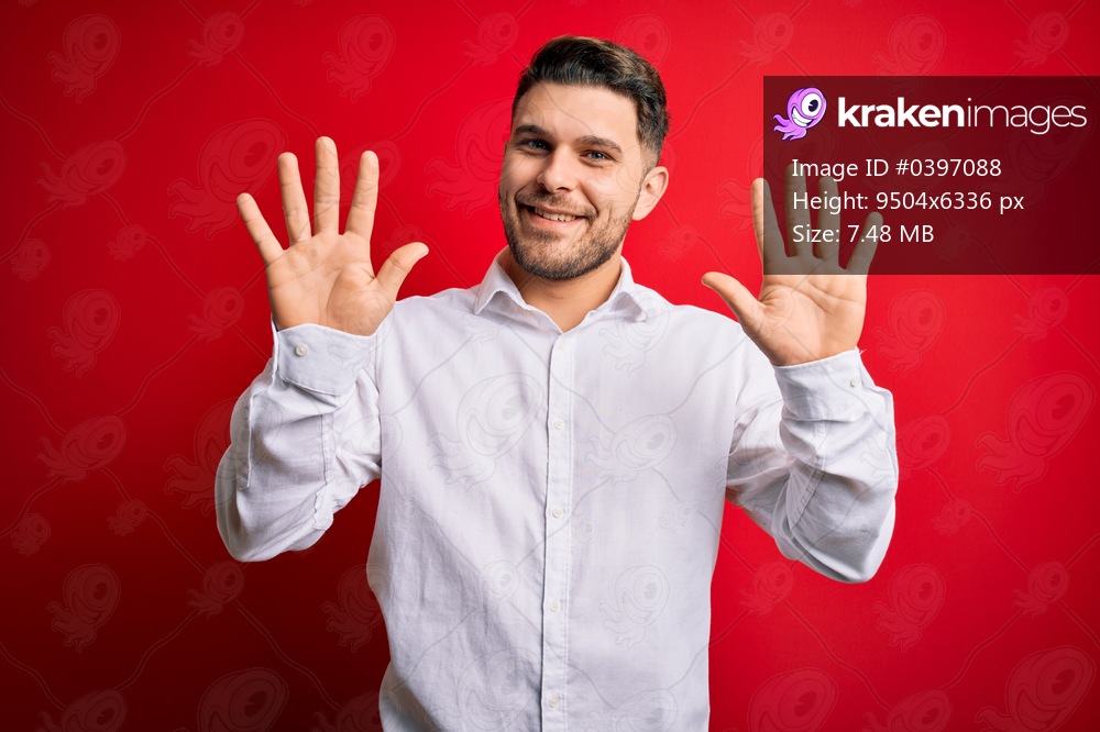 Young business man with blue eyes wearing elegant shirt standing over red isolated background showing and pointing up with fingers number ten while smiling confident and happy.
