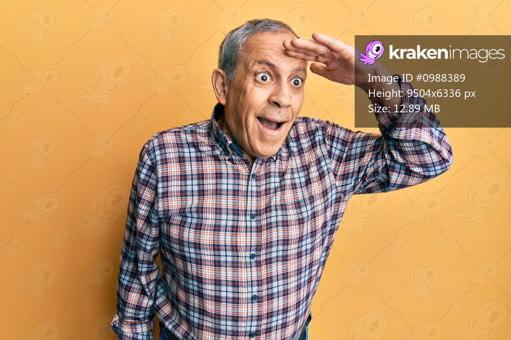 Handsome senior man with grey hair wearing casual shirt very happy and smiling looking far away with hand over head. searching concept. 