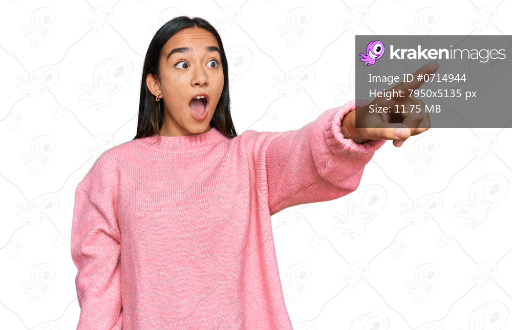 Young asian woman wearing casual winter sweater pointing with finger surprised ahead, open mouth amazed expression, something on the front 