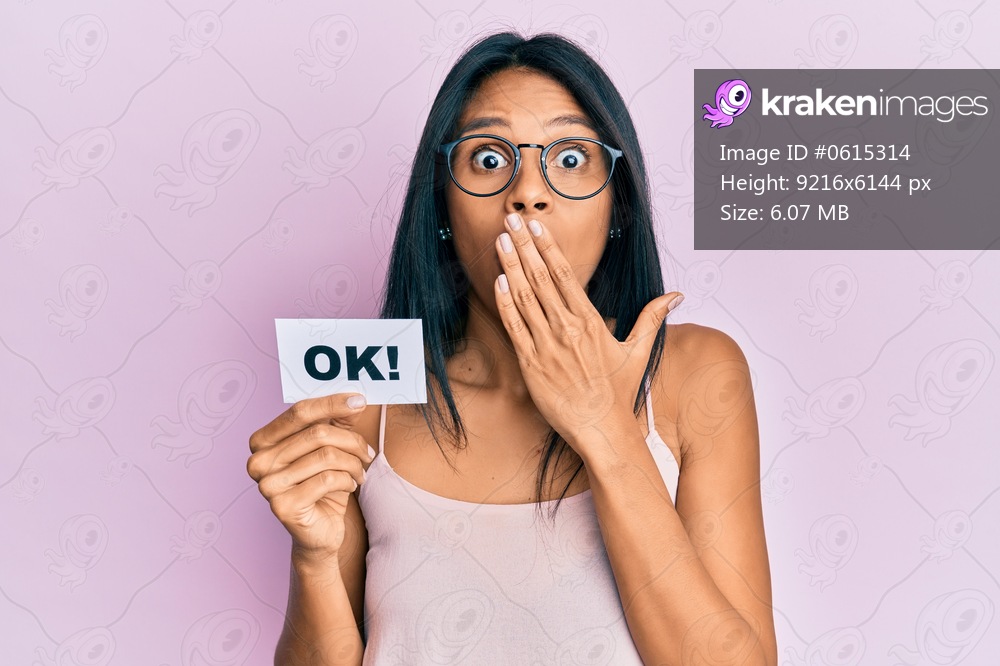 Young african american woman holding ok message paper covering mouth with hand, shocked and afraid for mistake. surprised expression 