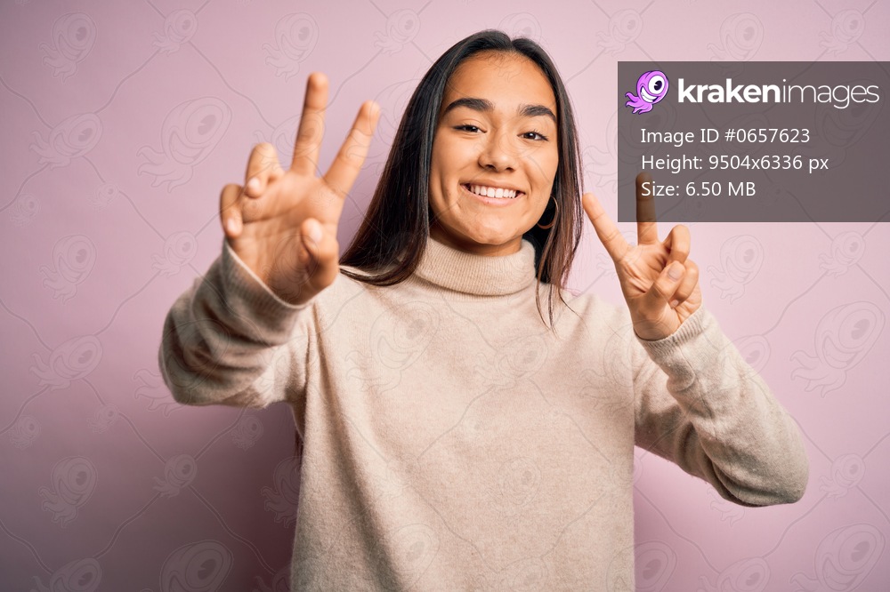 Young beautiful asian woman wearing casual turtleneck sweater over pink background smiling looking to the camera showing fingers doing victory sign. Number two.