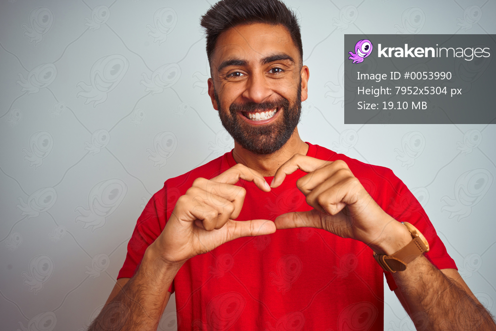 Young indian man wearing red t-shirt over isolated white background smiling in love showing heart symbol and shape with hands. Romantic concept.