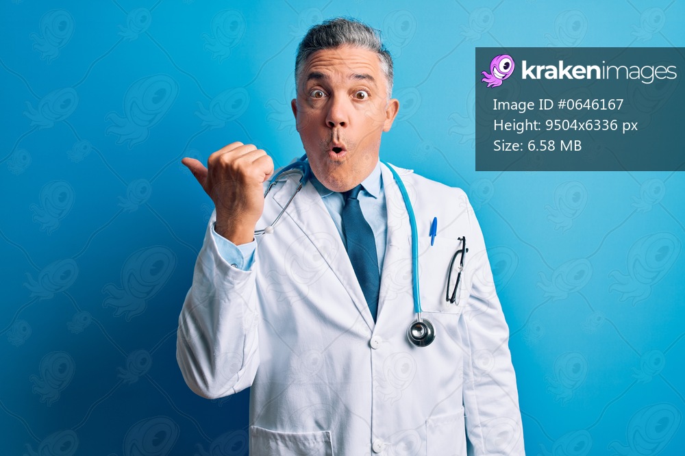Middle age handsome grey-haired doctor man wearing coat and blue stethoscope Surprised pointing with hand finger to the side, open mouth amazed expression.