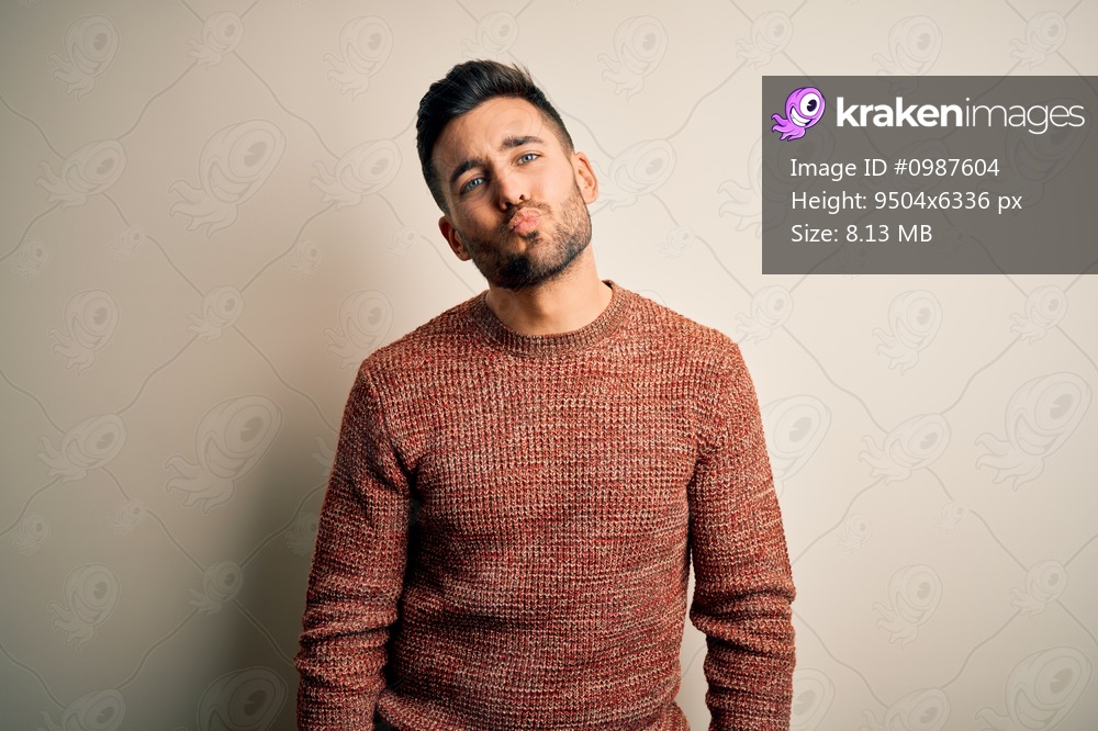 Young handsome man wearing casual sweater standing over isolated white background looking at the camera blowing a kiss on air being lovely and sexy. Love expression.