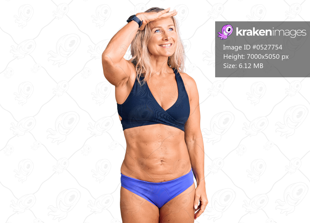 Middle age fit blonde woman wearing bikini very happy and smiling looking far away with hand over head. searching concept. 