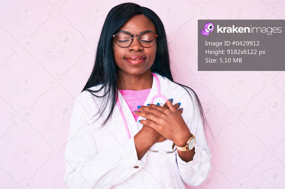 Young african american woman wearing doctor stethoscope smiling with hands on chest with closed eyes and grateful gesture on face. health concept. 