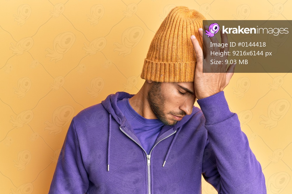 Young handsome man wearing wool winter hat surprised with hand on head for mistake, remember error. forgot, bad memory concept. 