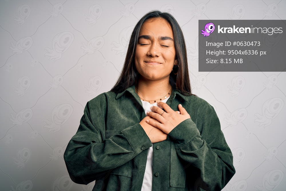 Young beautiful asian woman wearing casual shirt standing over isolated white background smiling with hands on chest with closed eyes and grateful gesture on face. Health concept.