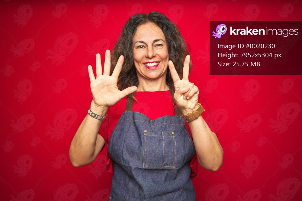 Middle age senior woman wearing apron uniform over red isolated background showing and pointing up with fingers number seven while smiling confident and happy.