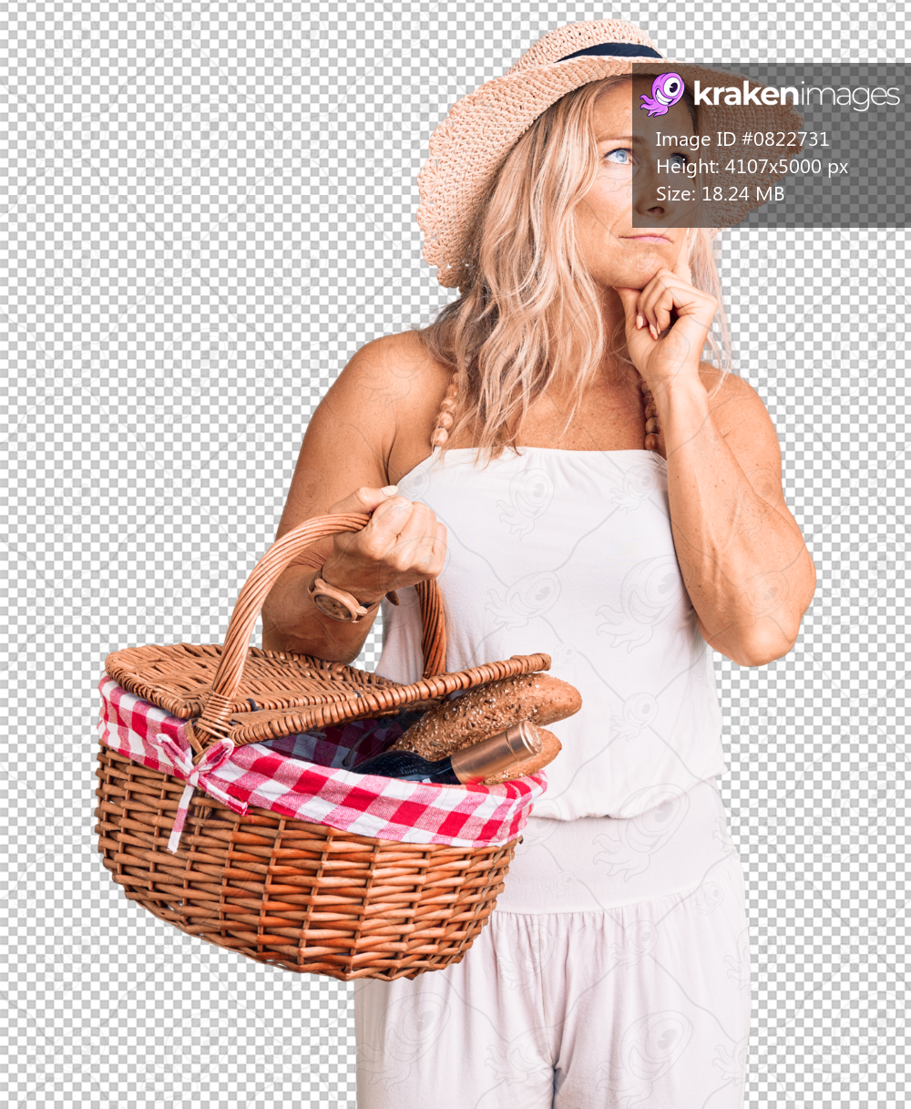 Middle age fit blonde woman wearing summer hat and holding picnic wicker basket with bread serious face thinking about question with hand on chin, thoughtful about confusing idea