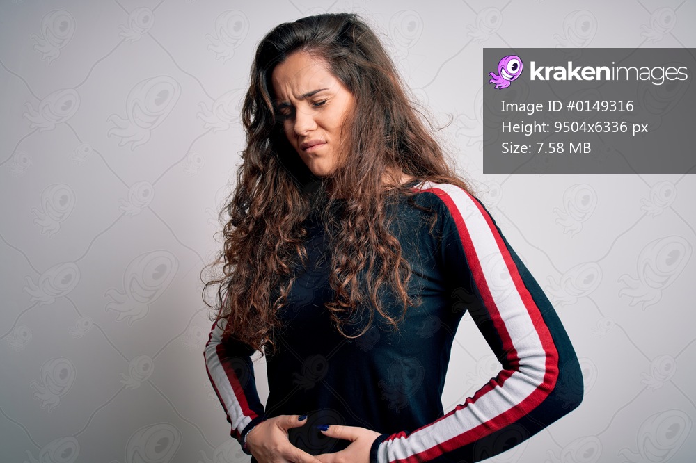Young beautiful woman with curly hair wearing casual sweater over isolated white background with hand on stomach because indigestion, painful illness feeling unwell. Ache concept.