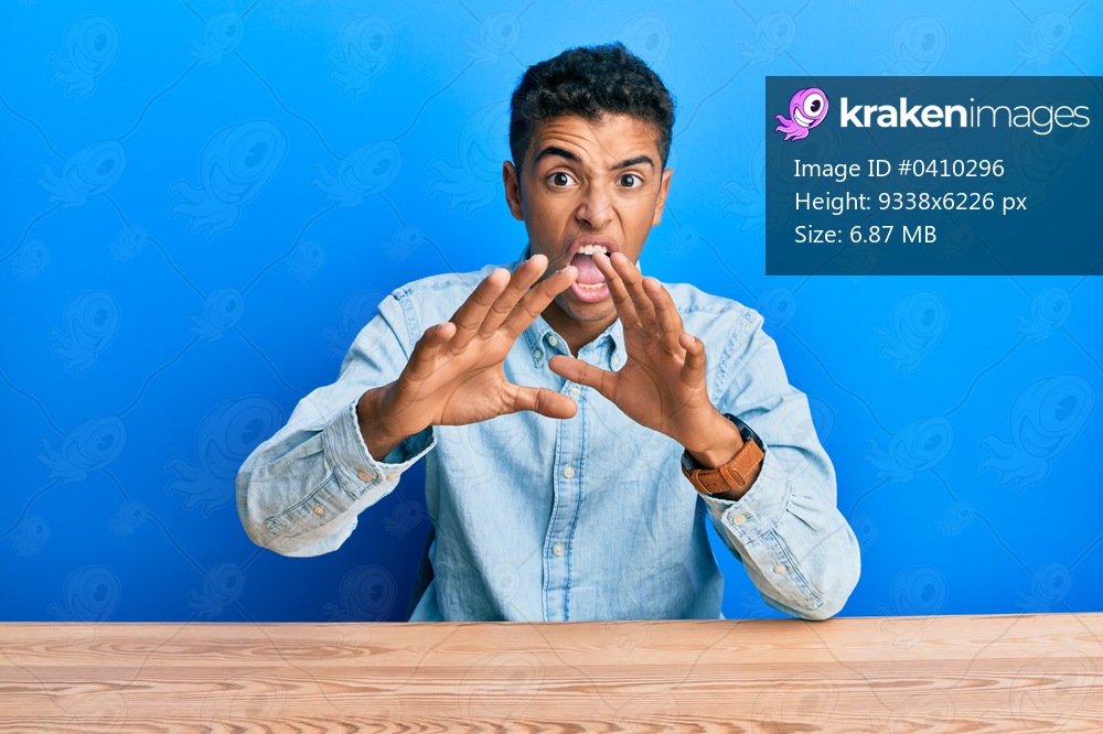 Young handsome african american man wearing casual clothes sitting on the table afraid and terrified with fear expression stop gesture with hands, shouting in shock. panic concept. 