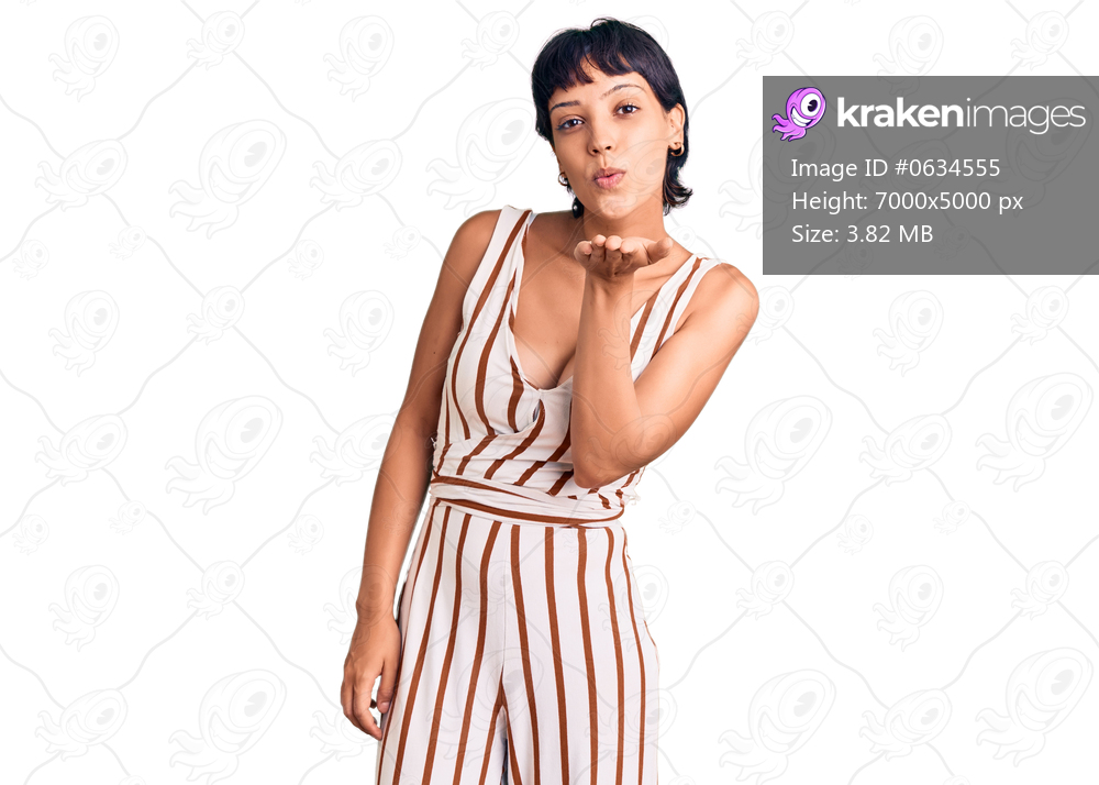 Young brunette woman with short hair wearing summer outfit looking at the camera blowing a kiss with hand on air being lovely and sexy. love expression. 