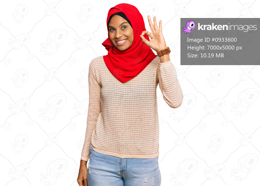 Young african american woman wearing traditional islamic hijab scarf smiling positive doing ok sign with hand and fingers. successful expression. 