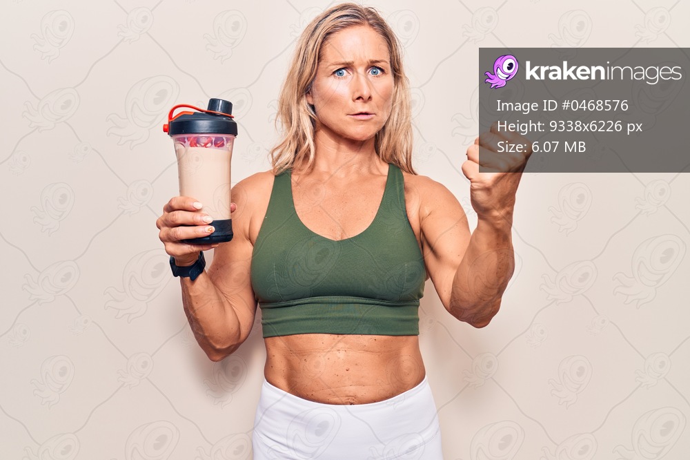 Middle age caucasian blonde woman wearing sport clothes drinking a protein shake annoyed and frustrated shouting with anger, yelling crazy with anger and hand raised 