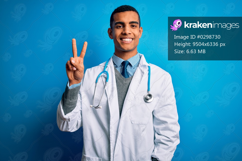 Handsome african american doctor man wearing coat and stethoscope over blue background smiling looking to the camera showing fingers doing victory sign. Number two.