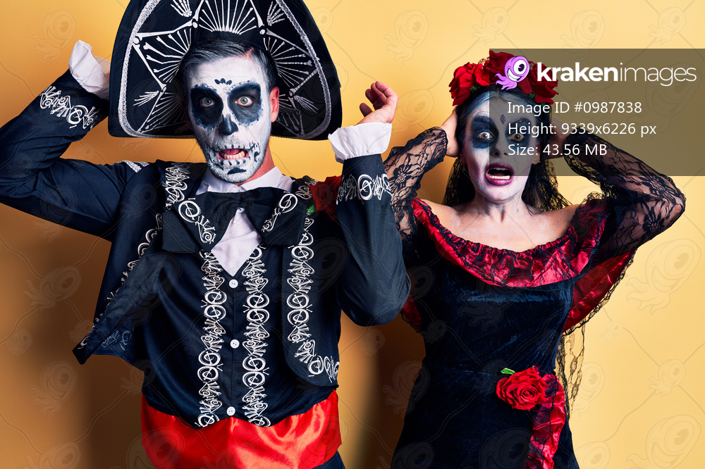 Young couple wearing mexican day of the dead costume over yellow crazy and scared with hands on head, afraid and surprised of shock with open mouth 