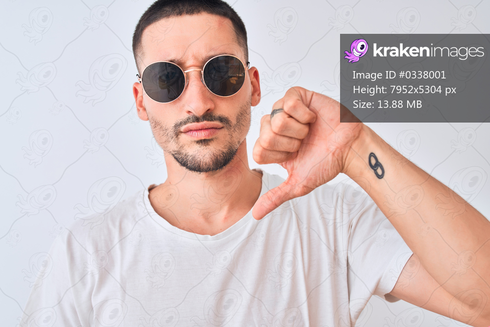 Young handsome man wearing sunglasses and casual t-shirt over isolated background with angry face, negative sign showing dislike with thumbs down, rejection concept