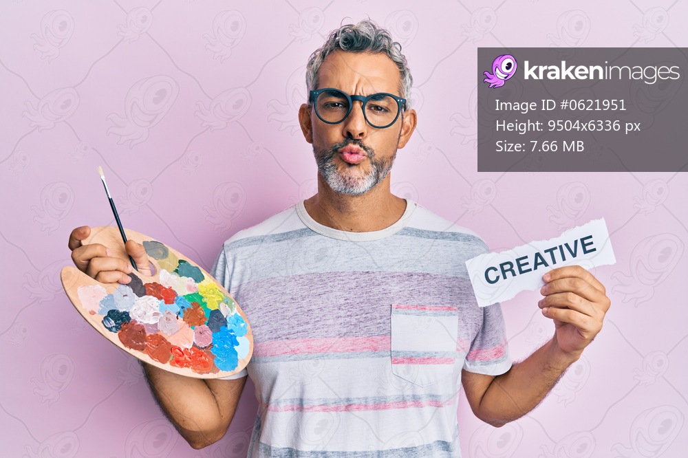 Middle age grey-haired man holding palette and creative message paper looking at the camera blowing a kiss being lovely and sexy. love expression. 