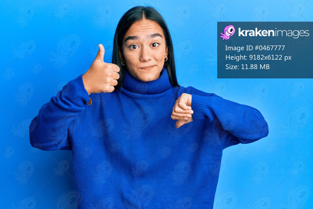 Young asian woman wearing casual winter sweater doing thumbs up and down, disagreement and agreement expression. crazy conflict 