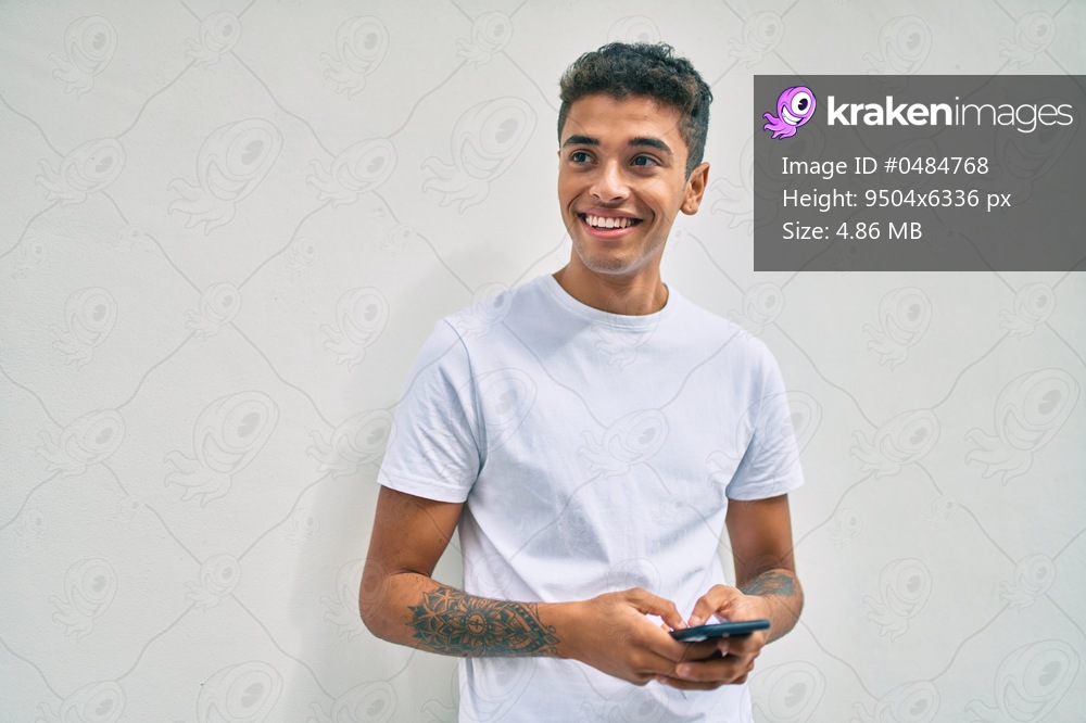Young latin man smiling happy using smartphone walking at the city.